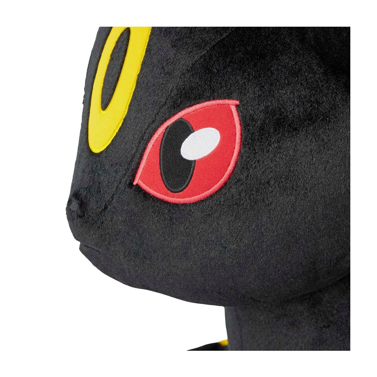 Close-up of a black plush toy with red and yellow eyes on a white background
