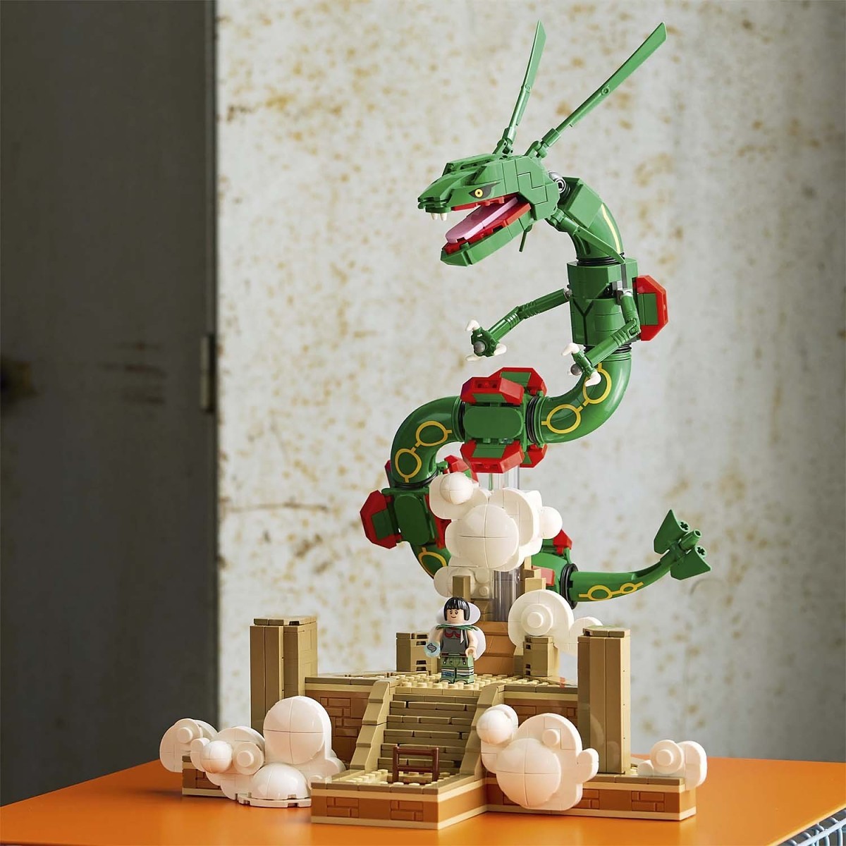 A green dragon-shaped building block set displayed on a table, featuring a small LEGO minifigure, white cloud pieces, and a tan base against a textured wall background.